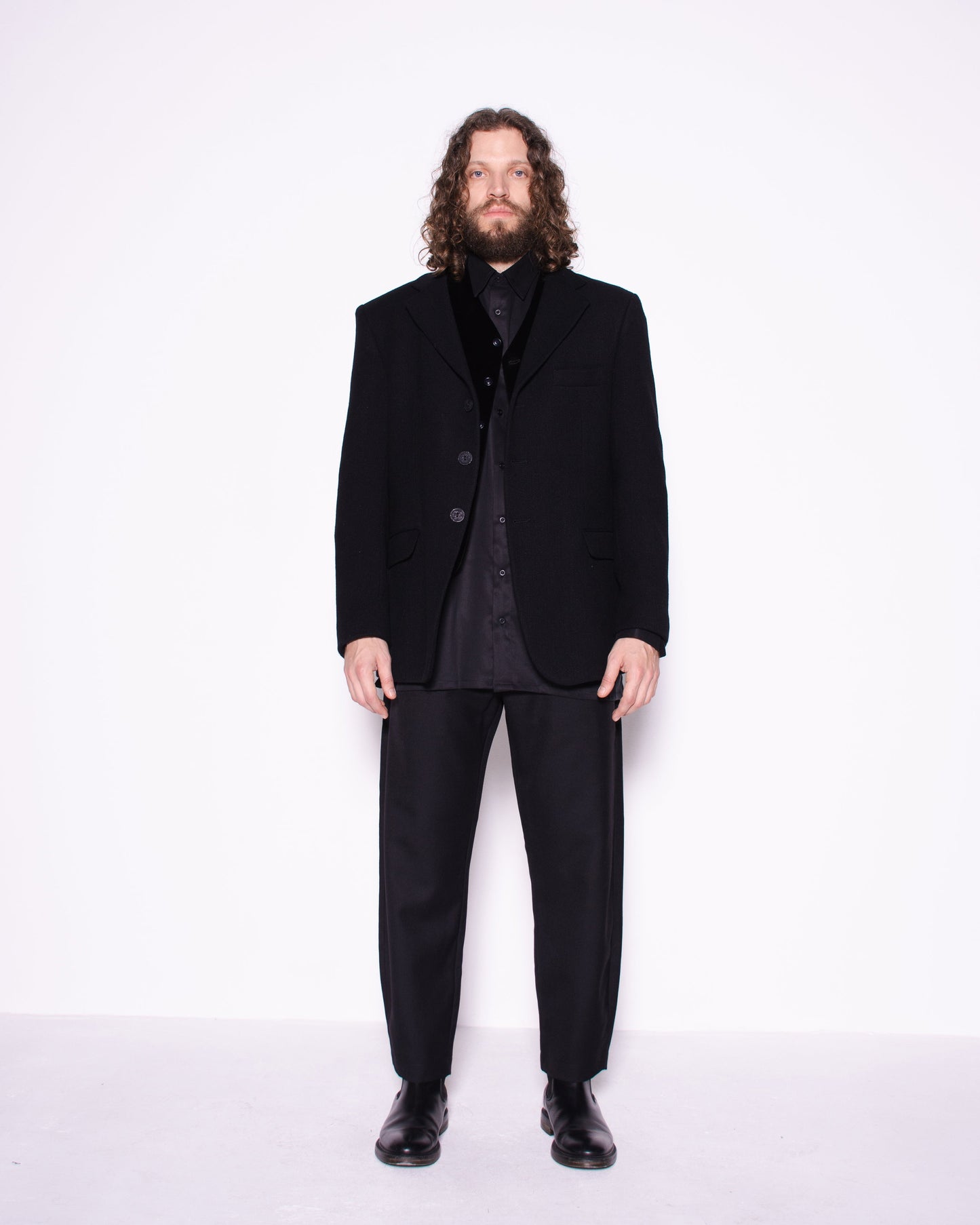 Man wearing a black suit standing against a white background