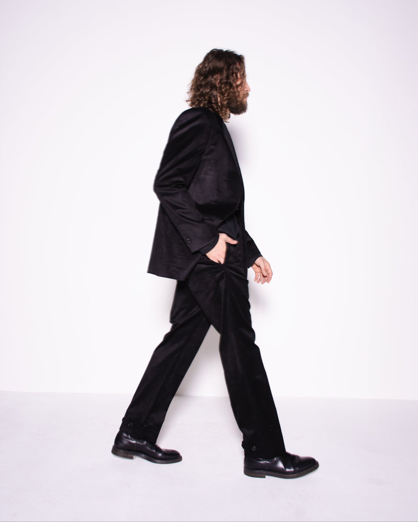 Person wearing a black suit walking on a white background