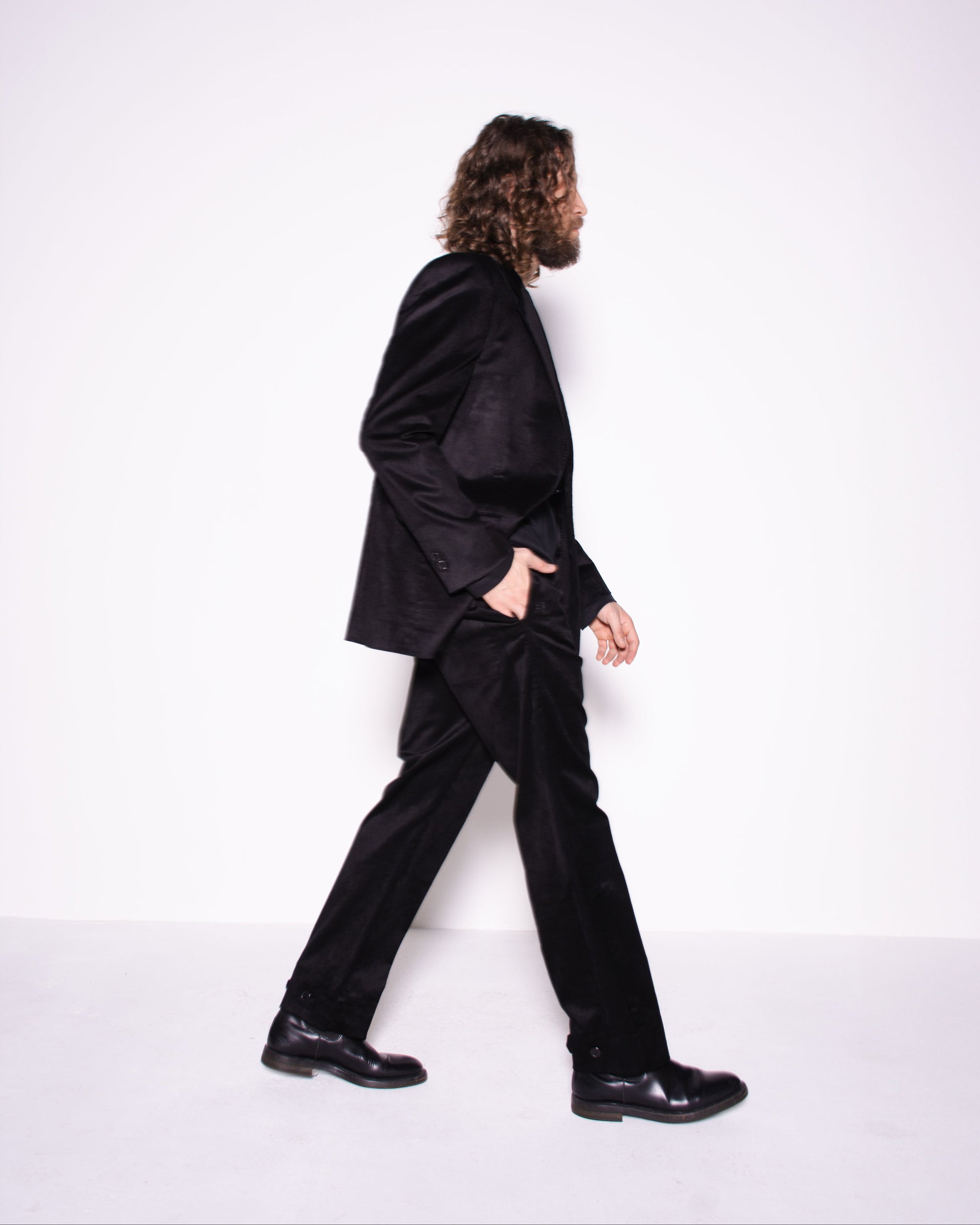 Person wearing a black suit walking on a white background