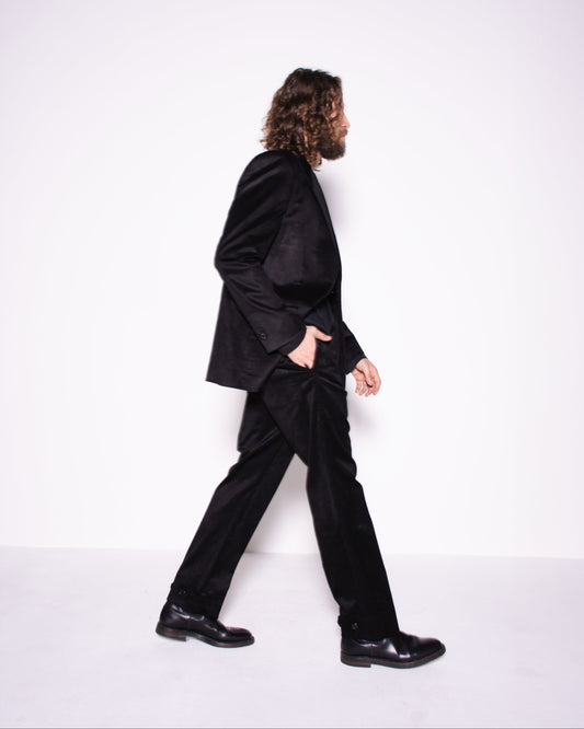 Person wearing a black suit walking on a white background
