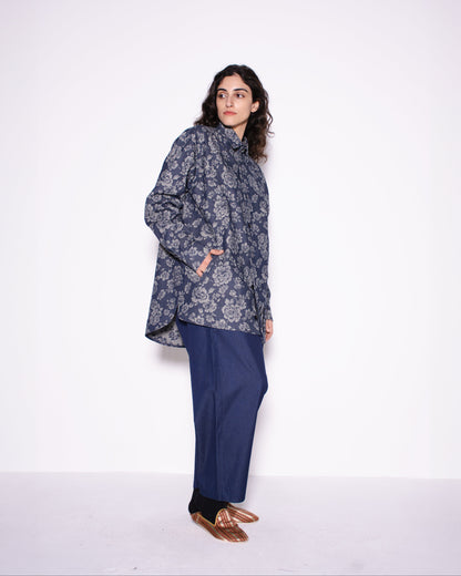 Person wearing a patterned coat and blue pants on a white background