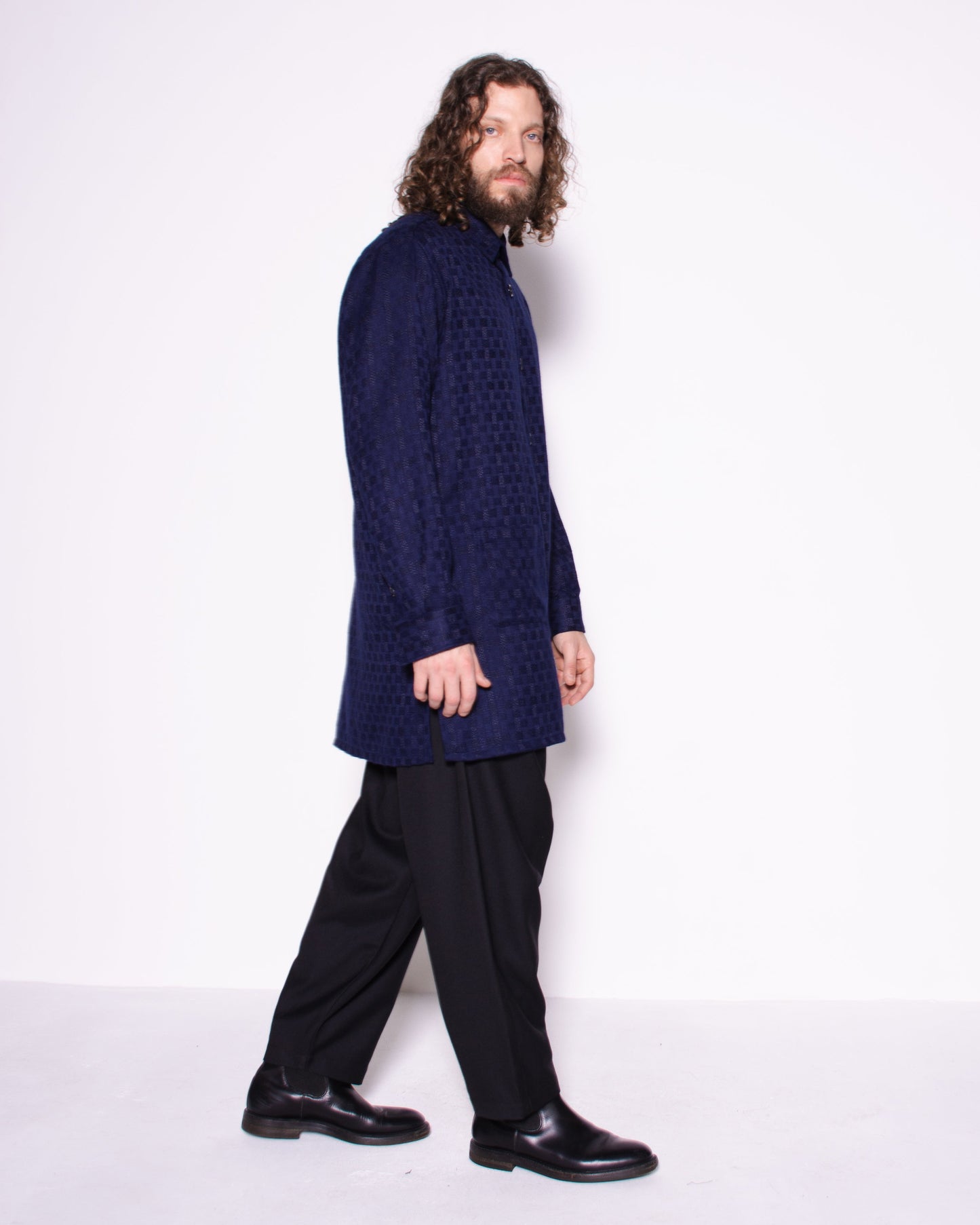 Person wearing a dark blue cable knit shirt and black pants on a white background