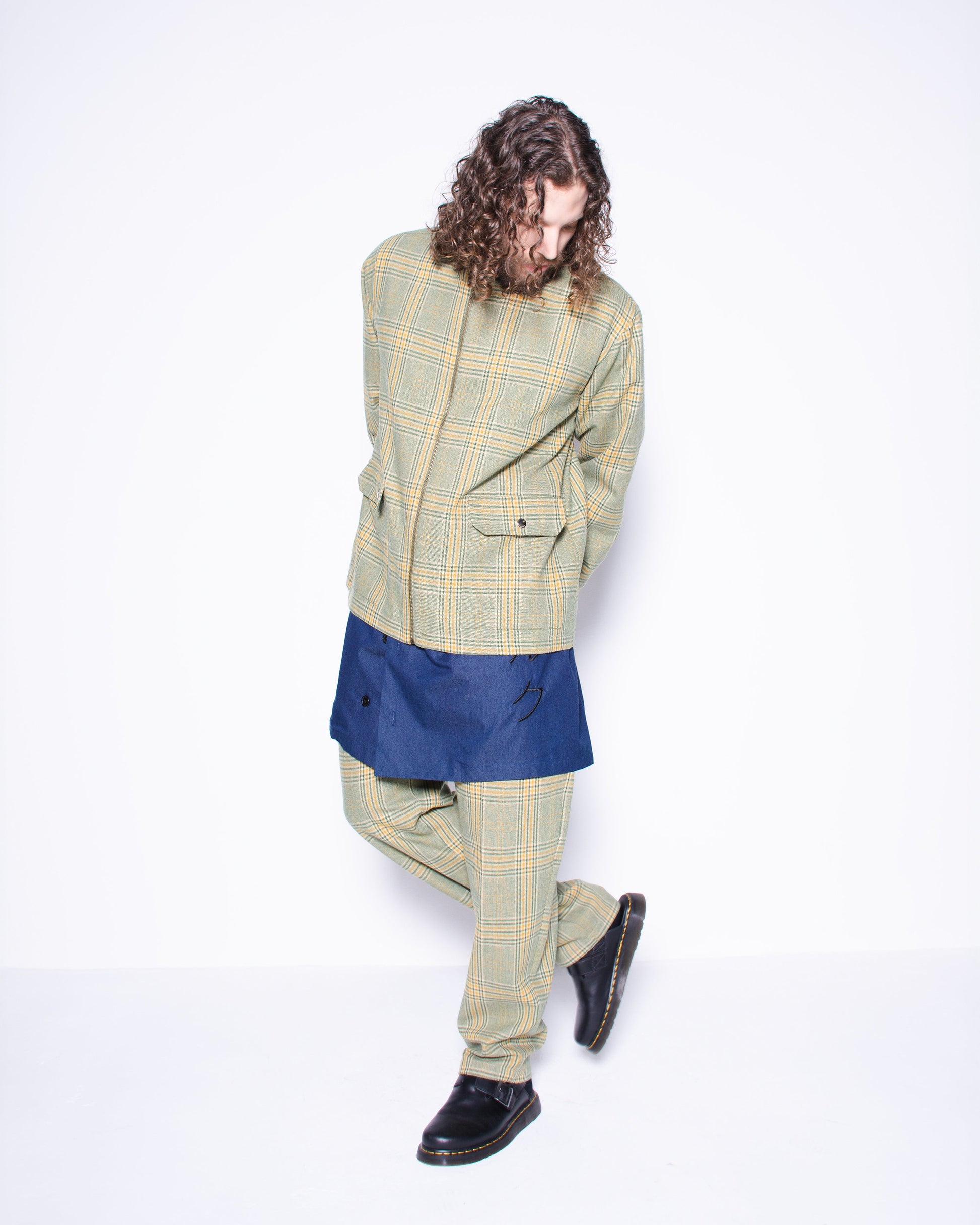  Person wearing green english wool striped  plaid coat and pants with a blue skirt underneath on a white background