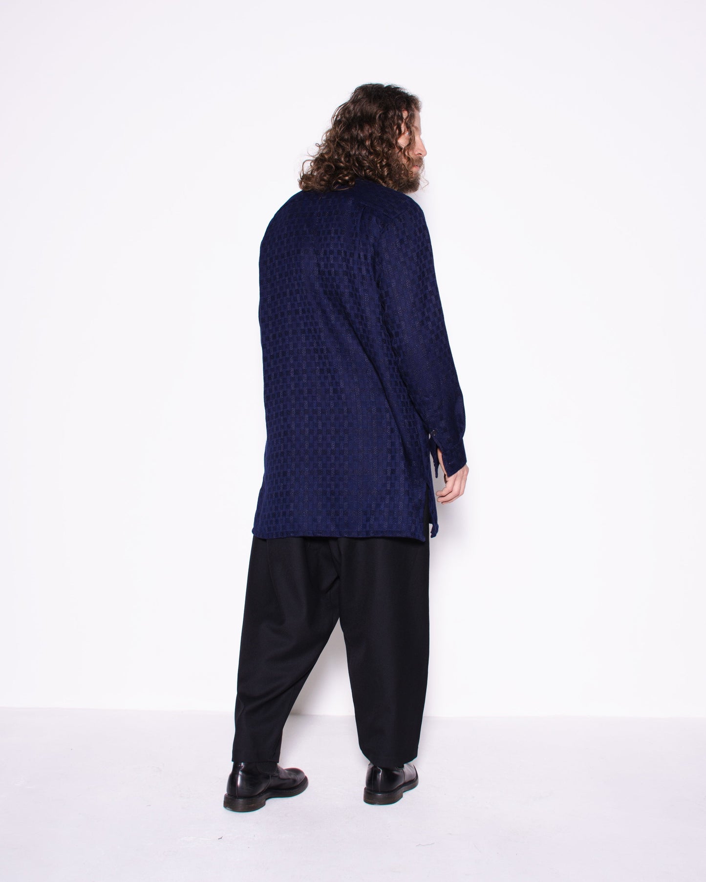 Person wearing a long dark blue shirt and black pants on a white background