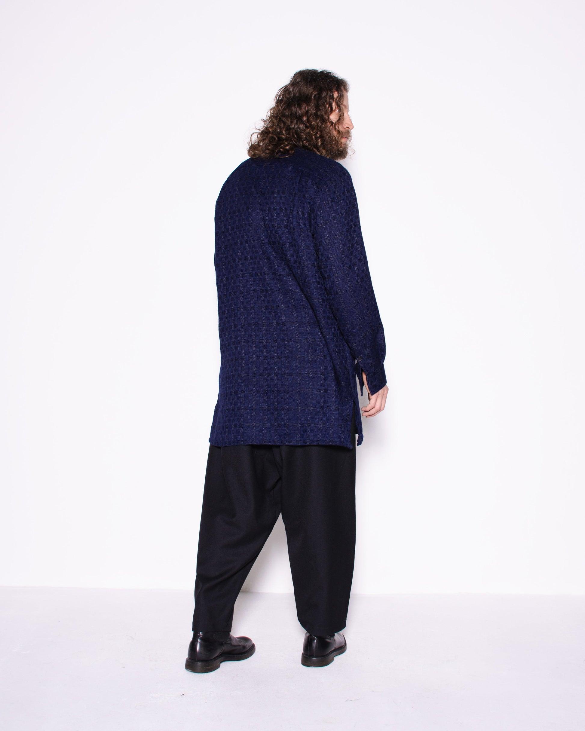 Person wearing a long dark blue shirt and black pants on a white background