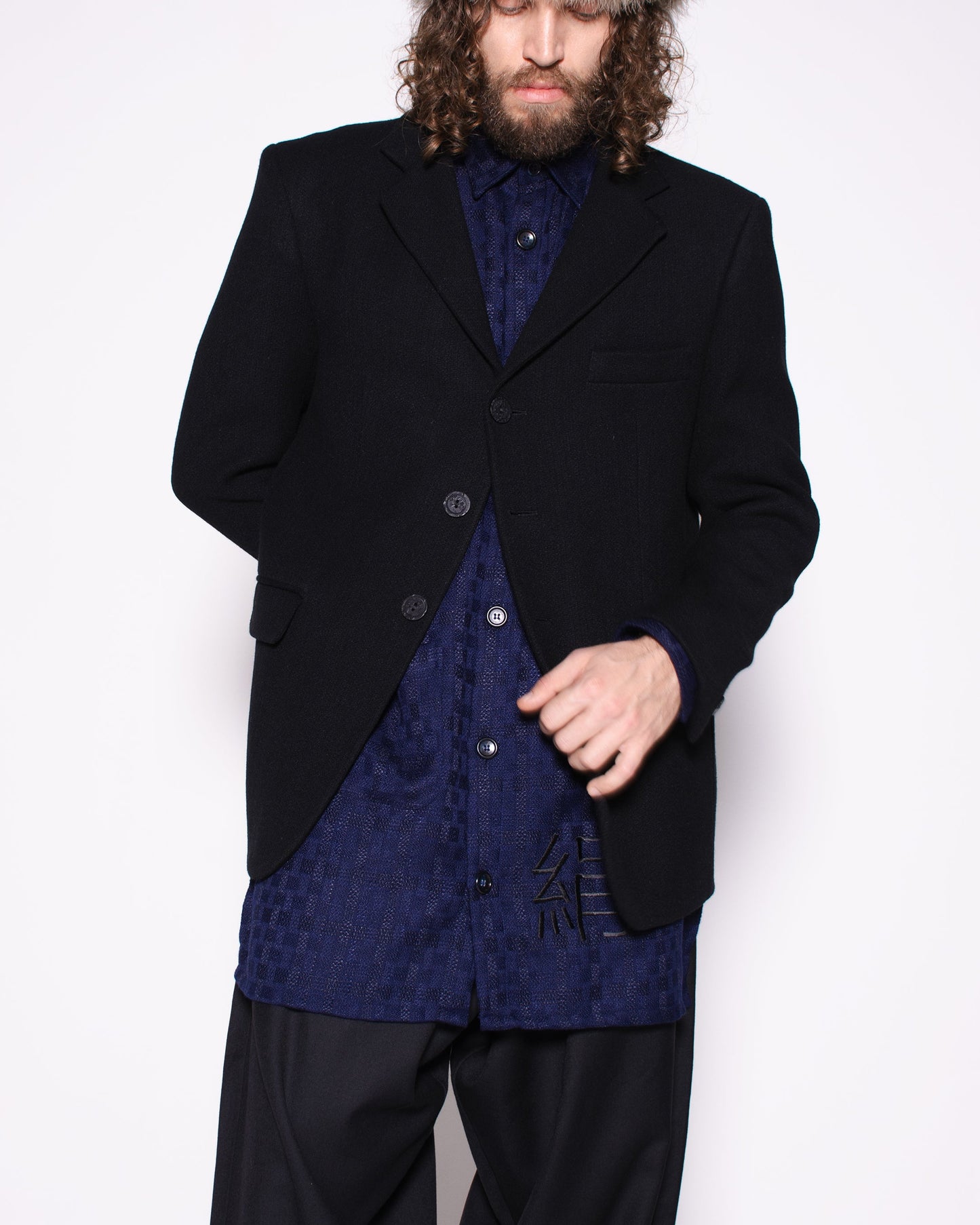 Person wearing a dark coat, fur hat, and patterned shirt on a white background