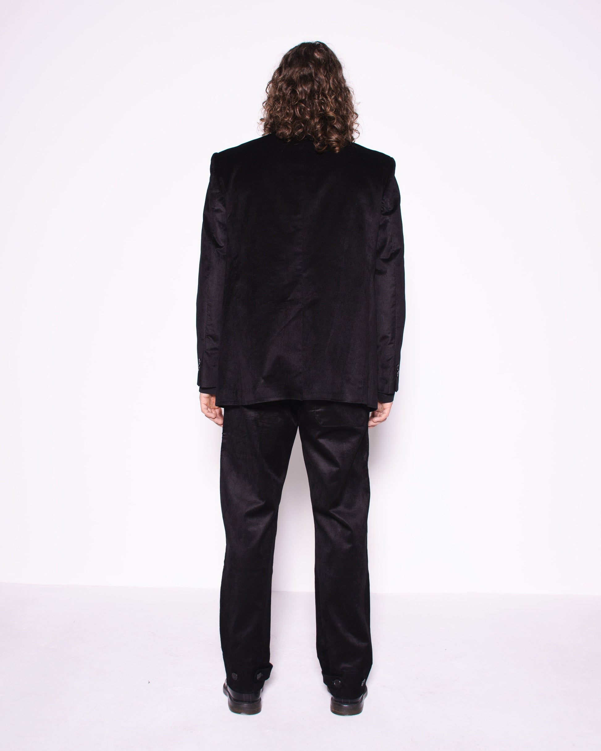 Person wearing a black suit standing against a white background